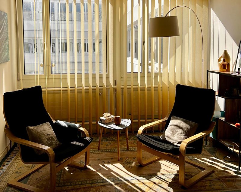La pièce de consultation baignée de soleil : deux fauteuils face à face autour d'une petite table, une lampe et une étagère