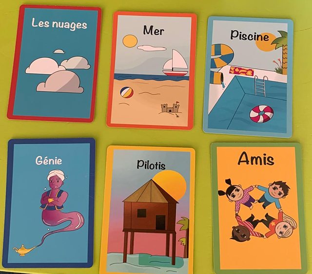 Six cartes illustrées posées sur une table : les nuages, la mer, une piscine, un génie, une maison sur pilotis, des amis