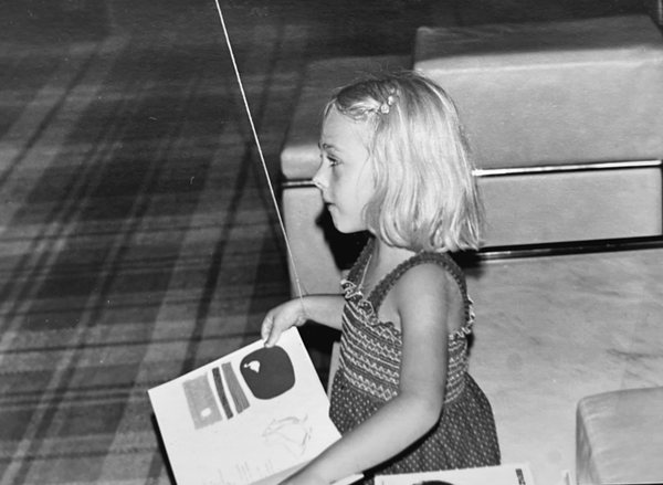 Luisa enfant, de profil, tenant un livre illustré, en noir et blanc