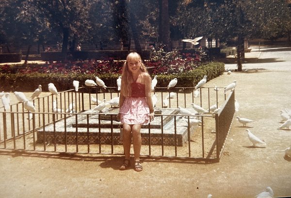 Luisa enfant, souriante, assise dans un parc au milieu de pigeons blancs
